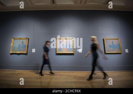 Members of staff walk past paintings of the Houses of Parliament by Claude Monet during a photocall for EY Exhibition: Impressionists in London, French Artists in Exile (1870-1904) which will unite the largest number of Monet's Houses of Parliament series seen in the UK for over forty years at the Tate Britain, London. Stock Photo