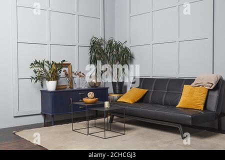 Bright apartment interior with black leather sofa, decorated wall lamp and table. Stock Photo