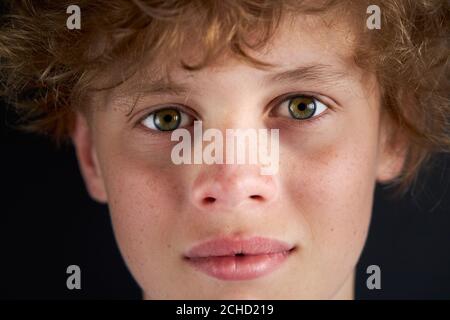 close-up portrait of calm caucasian boy looking at camera, male teenager isolated over black background Stock Photo