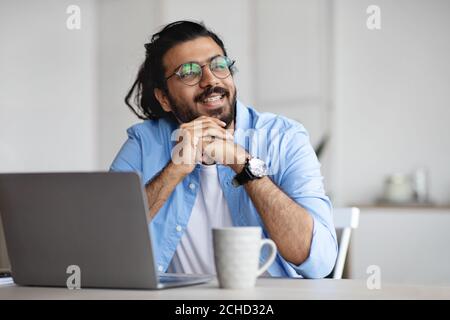 Pensive freelancer thinking about something while working on laptop at home office Stock Photo