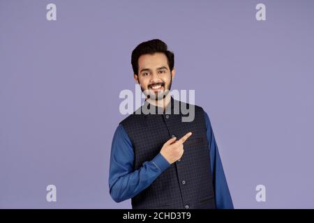 Handsome young Indian man smiling and pointing aside over lilac background Stock Photo