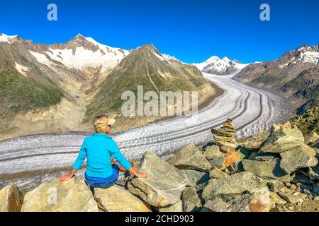 Hiker woman relaxing after trekking in Swiss Alps, Valais Canton, Switzerland, Europe. Woman looking Aletsch Glacier from Eggishorn summit with capped Stock Photo