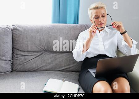 confident business lady wearing eyeglasses before work from home, she sits on sofa with laptop, in formal wear Stock Photo