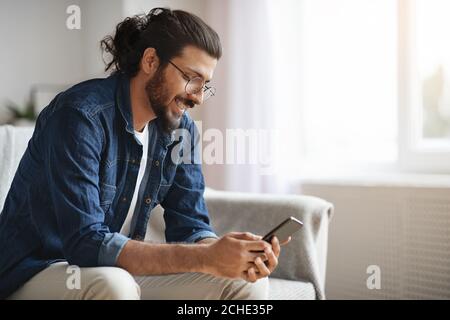New Mobile App. Stylish Western Guy Using Smatphone At Home, Browsing Internet Stock Photo