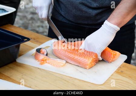 Man hands cutting pink raw salmon with knife on white board Stock Photo