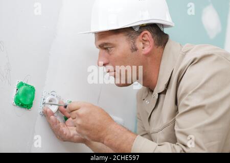 mature electrician installing socket on wall Stock Photo