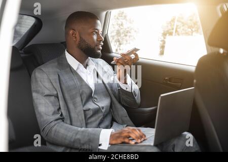 Black manager working on laptop in car, using phone Stock Photo