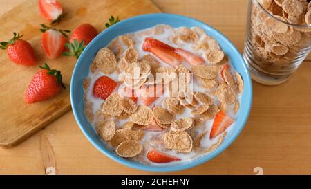 Whole grain flakes with milk and strawberries in blue bowl on wooden table. Healthy breakfast food Stock Photo