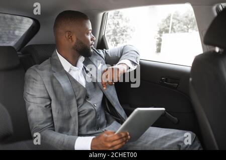 Thoughtful black guy entrepreneur using digital tablet in car Stock Photo