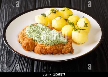 Portion of fried breaded schnitzel with boiled potatoes and Frankfurt green sauce close-up in a plate on the table. horizontal Stock Photo