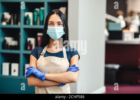 Beauty master in protective mask and gloves standing at hairdresser's interior, empty space Stock Photo