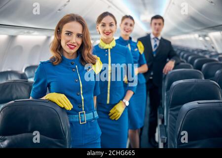 Happy cheerful aviation team in stylish blue and dark blue uniform standing in the salon of plane Stock Photo