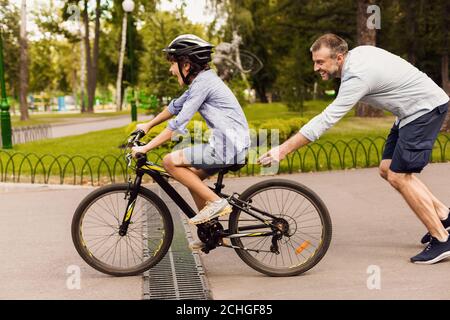 Son learning how to ride bicycle with his happy dad Stock Photo