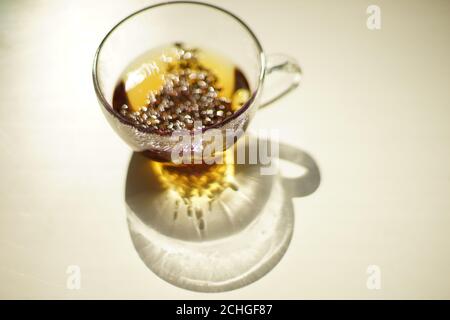Transparent glass cup with black flower tea on the sunny table. Stock Photo