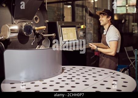 Cheerful young man using coffee roasting machine Stock Photo