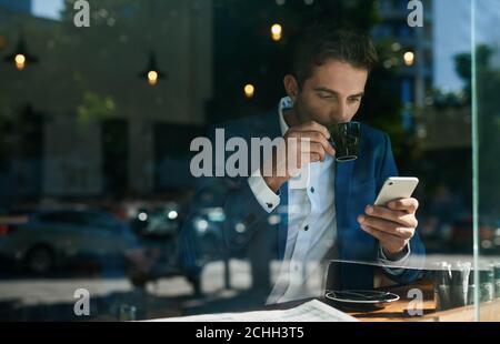 Businessman drinking coffee and checking his cellphone in a cafe Stock Photo