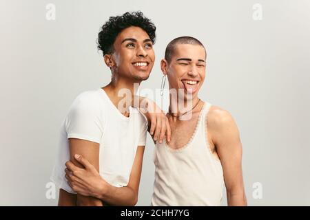 Gay male couple smiling on white background. Cheerful gender fluid couple standing together. Stock Photo