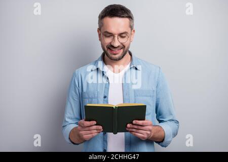 Close-up portrait of his he nice attractive cheerful cheery focused gray-haired guy reading interesting paper book isolated over gray light pastel Stock Photo