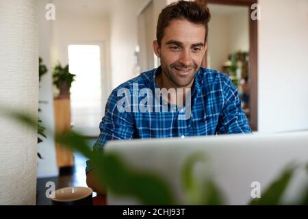 Smiling man using a laptop to work remotely from home Stock Photo