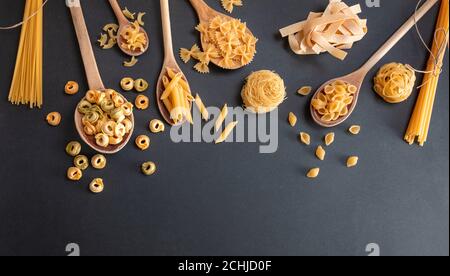 Pasta cooking concept. Raw pasta various shapes and spoons on black stone background, top view Stock Photo