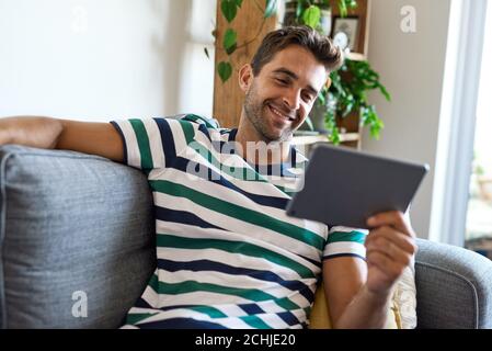 Smiling young man sitting at home using a digital tablet Stock Photo