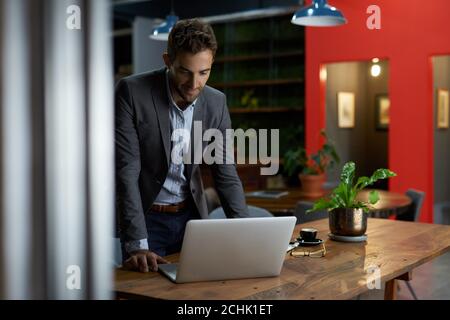 Businessman standing at his office desk working on a laptop Stock Photo