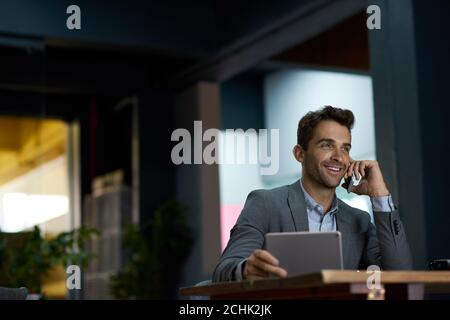 Smiling businessman using a tablet and talking on his cellphone Stock Photo