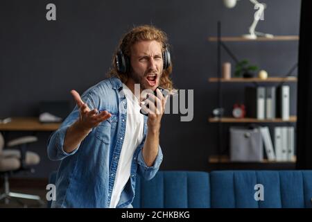 Handsome long haired curly man with headphones listening music,singing and dancing.Funny emotional smiling man with earphones and mobile phone relax Stock Photo
