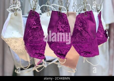 Purple and white lace fabric reusable face masks hanging on clothes hanger.Making cloth mask to prevent the outbreak of Covid-19 virus become popular. Stock Photo