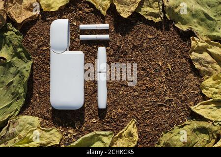 White battery  with  individual stick e-cigarette and cigarette for it  lies on  dry  tobacco texture with green, yellow  leaves  of tobacco. This is Stock Photo