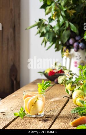 Autumn apple drink, apple slices with juice and mint in a glass on a wooden table, leaves in a vase, morning in the village, rustic concept Stock Photo