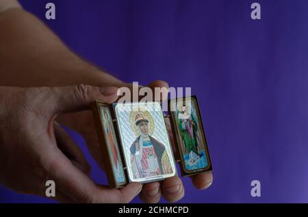 Hands hold the Christian icon of the sacred princess Olga and the archangels Gabriel and Michael. Male hands with an icon on a colored background. Ort Stock Photo