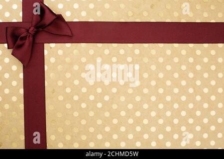 Abstract holiday gift background of craft paper with golden pin-up dots dotted with silk satin ribbon bow with copy space for text, luxury wine color Stock Photo