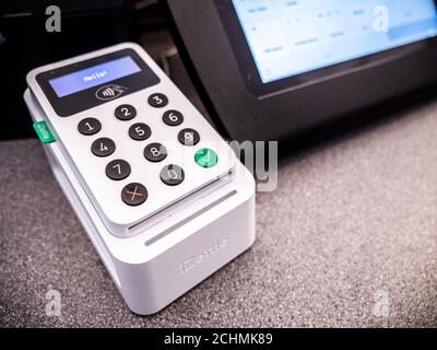 An iZettle branded POS (Point of Sale) credit/debit card reading machine on a shop counter with touch screen till in the background. Stock Photo
