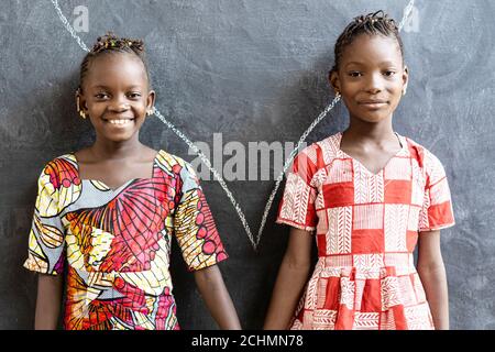 Gorgeous African Sisters Posing, Smiling and Laughing Happy in Front of Blackboard at School Stock Photo