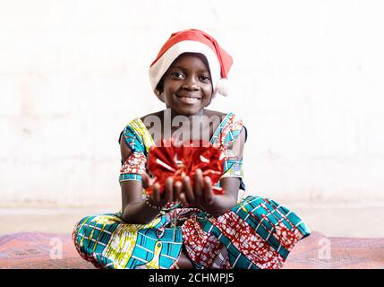 Cute Christmas African Black Girl with Funny Hat and Red Present at Home in Bamako, Mali Stock Photo