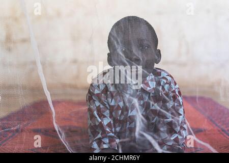 Smiling Cute Black Boy Portrait with Malaria Concept Covered by Mosquito Net Stock Photo