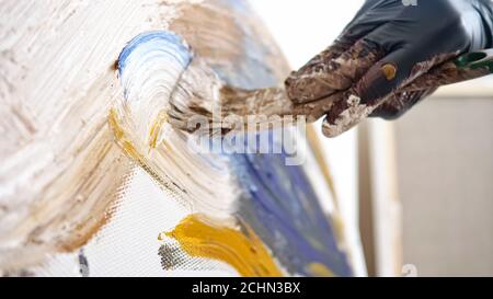 professional artist hand in black latex glove holds brush and draws on canvas with coloured paints at home on summer day close view Stock Photo