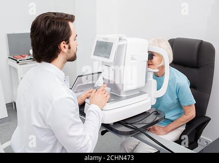 Practicing ophthalmologist examines a senior woman patient's with special ophthalmic equipment in a modern clinic. Vision correction of elderly people Stock Photo