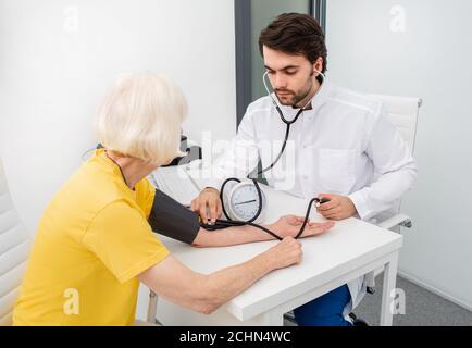 doctor therapist in modern clinic measures body pressure of an senior woman. Prevention of diseases of hypertension, atherosclerosis and heart failure Stock Photo