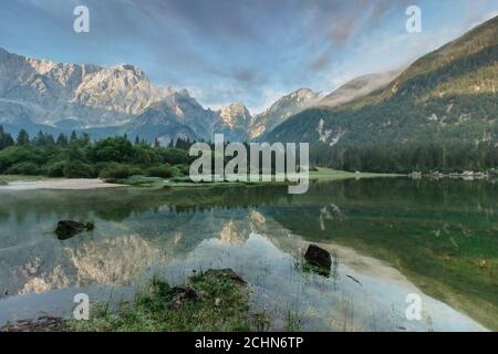 Mirror reflection in Lago di Fusine, Italy. Summer spring colors and Mangart mountain in the background at sunrise in Italien Alps.Beautiful peaceful Stock Photo