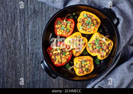 stuffed bell peppers with ground beef, corn and cheese in a black baking dish on a wooden table, horizontal view from above, flat lay, free space Stock Photo