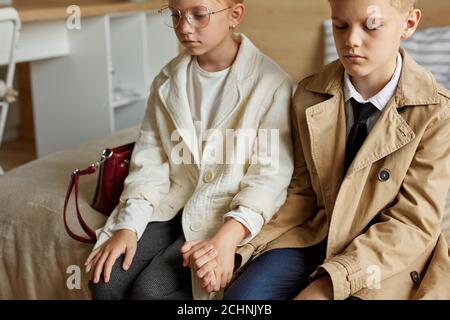 tired kids couple waiting for their taxi in hotel, want to sleep, sad redhead girl and boy sit on bed in coats with bags Stock Photo