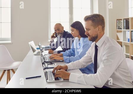 Company employees sitting at office desk, working on laptops, doing research and collecting data Stock Photo