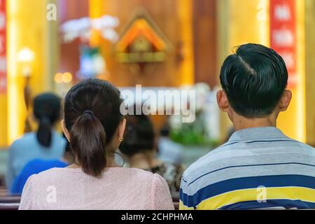 A blurred background photo of the inside of a Vietnamese church sanctuary that is filled with people in the pews, and the pastor stands under a large Stock Photo