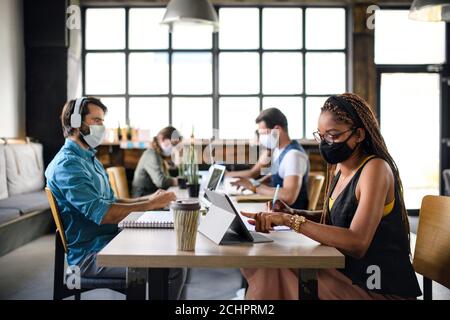 Business people with face masks indoors in office, back to work after coronavirus lockdown. Stock Photo