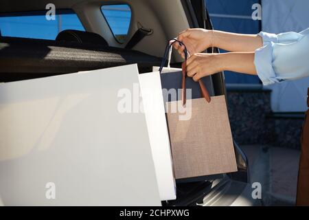 Close up of unrecognizable young woman loading shopping bags in car trunk on parking lot by mall, copy space Stock Photo