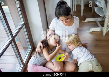 Small children hugging pregnant belly of mother expecting baby indoors at home. Stock Photo