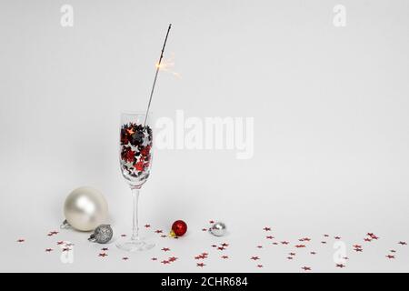 Glasses of champagne with confetti in shape of stars and sparkler on white background, Christmas decorations around, copy space. Concepts of greeting Stock Photo