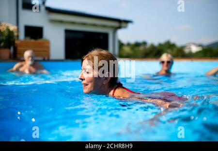 Portrait of senior woman in swimming pool outdoors in backyard. Stock Photo